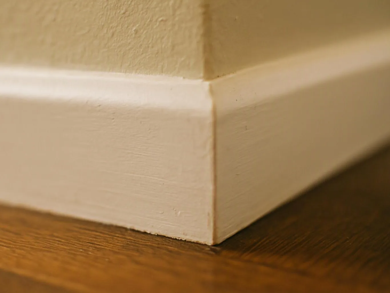 Close-up of a beige wall corner with white baseboard trim meeting a wood floor