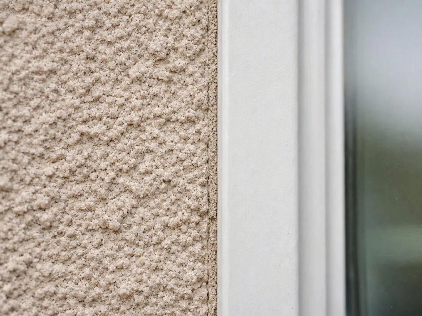 Close-up of a textured beige wall beside a white window frame and frosted glass pane
