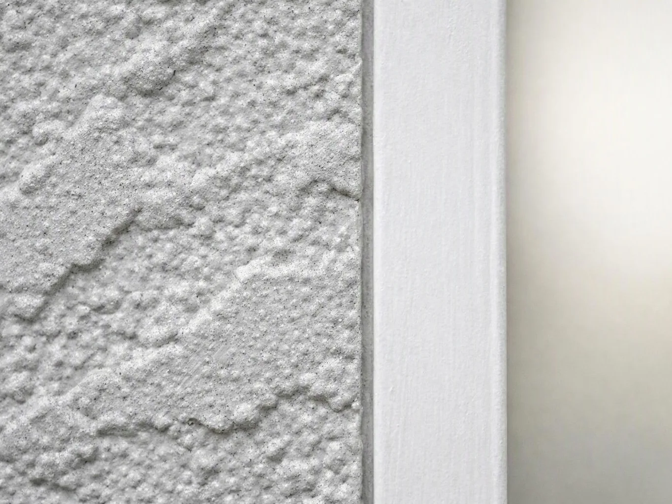 Close-up of a textured gray wall beside a white trim strip and pale wall panel