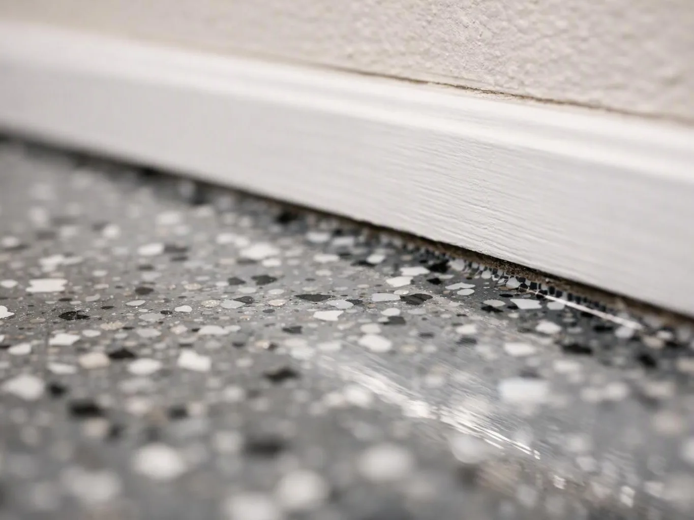 Close-up of a white baseboard above a speckled gray floor with a narrow gap between them