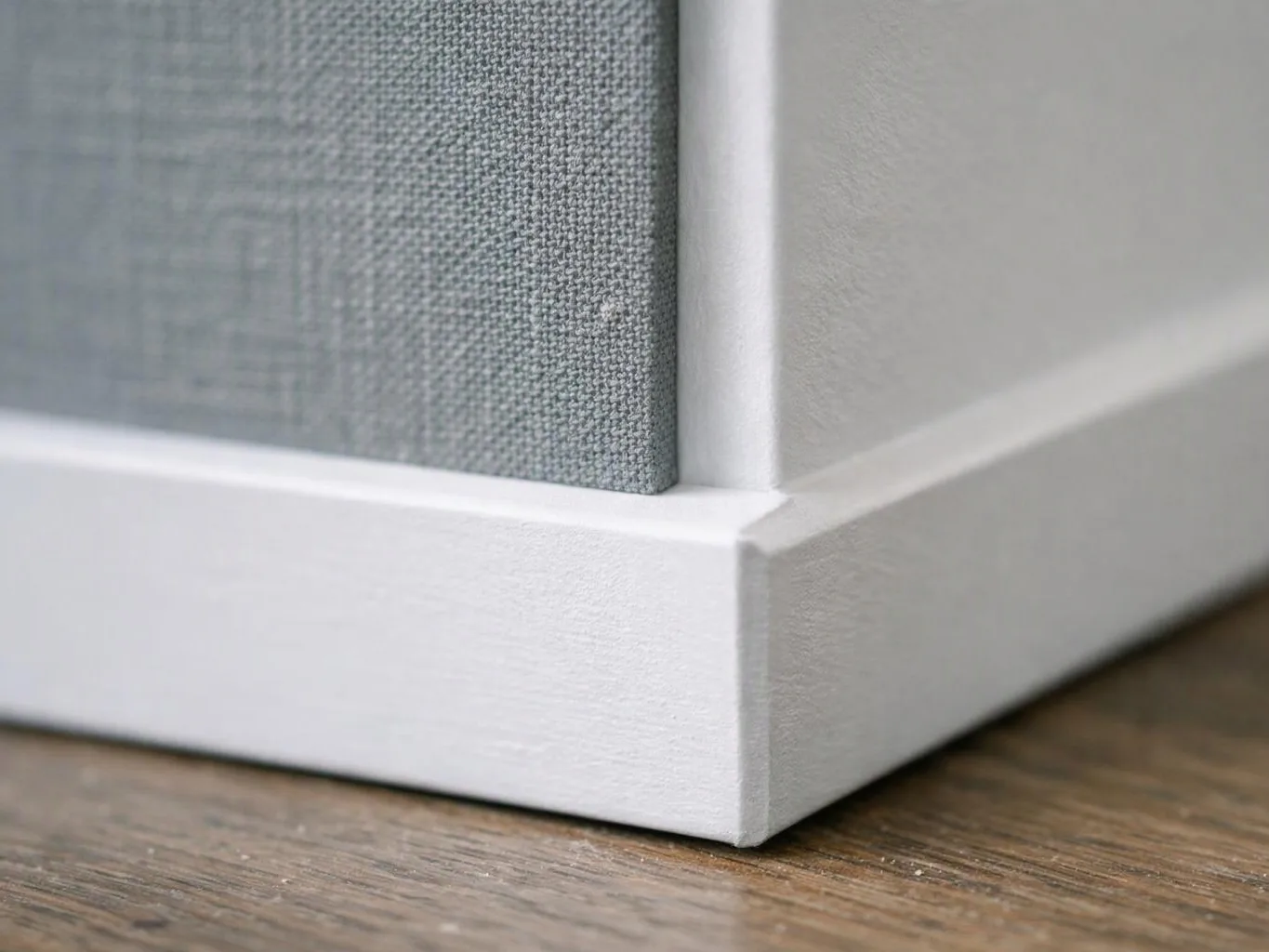 Close-up of a white canvas frame corner with gray fabric on a wooden surface