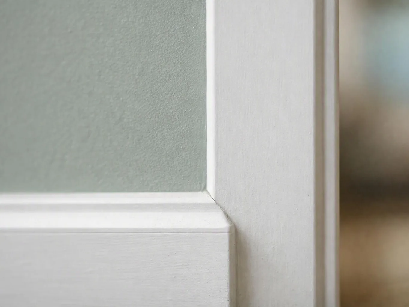 Close-up of a white painted door frame beside a textured pale green wall
