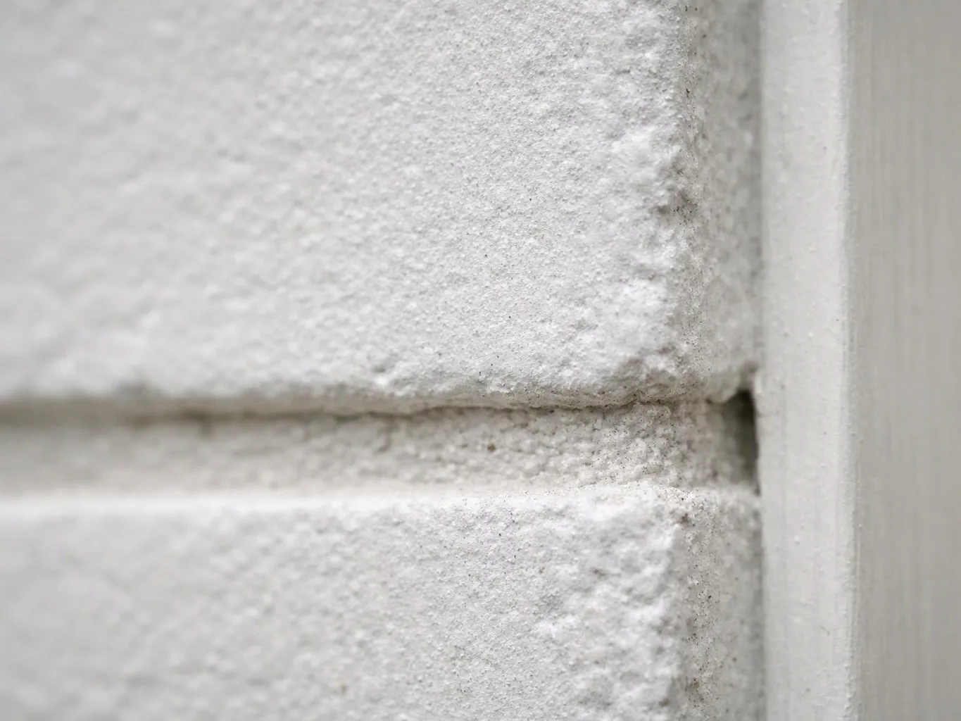 Close-up of a white textured painted brick wall meeting a smooth trim edge with a narrow gap