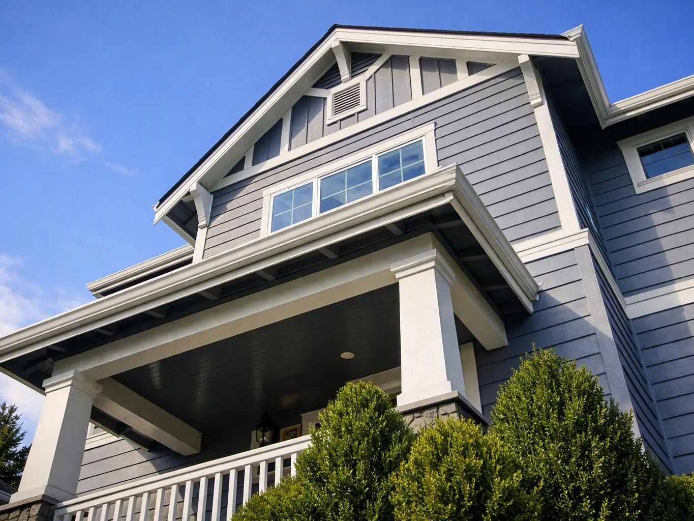 A gray two-story house with white trim and a covered porch stands under a clear blue sky
